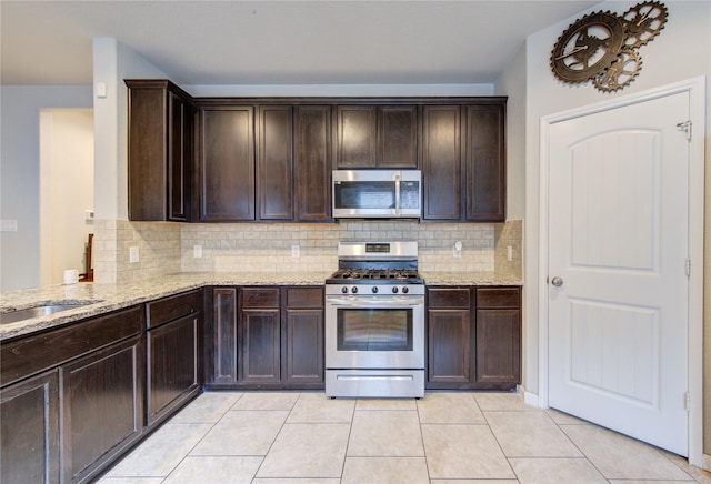 kitchen with stainless steel appliances, light stone counters, dark brown cabinets, and tasteful backsplash