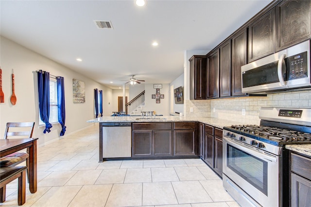 kitchen with appliances with stainless steel finishes, backsplash, a sink, a peninsula, and dark brown cabinetry