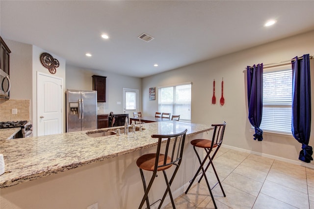 kitchen featuring stainless steel appliances, a sink, recessed lighting, a breakfast bar, and light stone counters