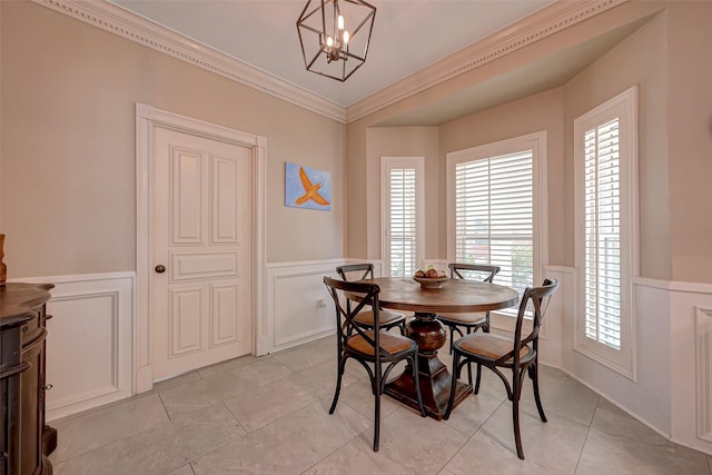 dining area featuring a wainscoted wall, a decorative wall, ornamental molding, a chandelier, and light tile patterned floors