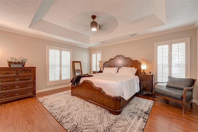 bedroom with a tray ceiling, light wood-style flooring, baseboards, a ceiling fan, and ornamental molding
