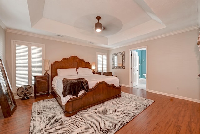 bedroom featuring a tray ceiling, wood finished floors, baseboards, and crown molding