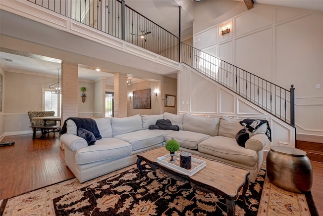 living area featuring wood-type flooring, a decorative wall, crown molding, baseboards, and a towering ceiling