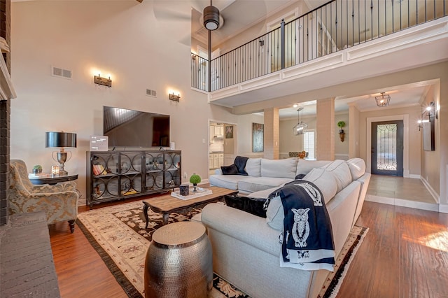 living area with wood finished floors, baseboards, a high ceiling, crown molding, and ceiling fan
