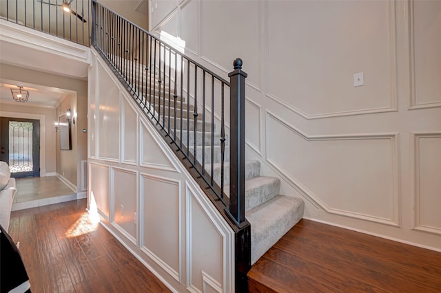 stairway with a decorative wall, wood finished floors, baseboards, and ornamental molding