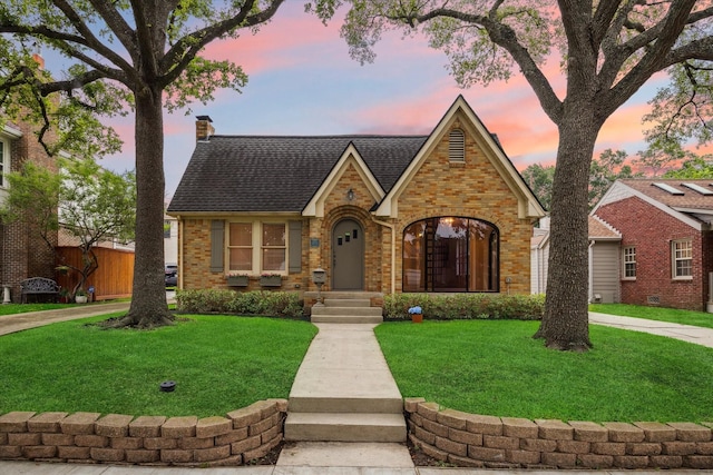 tudor home featuring a chimney, brick siding, and a shingled roof