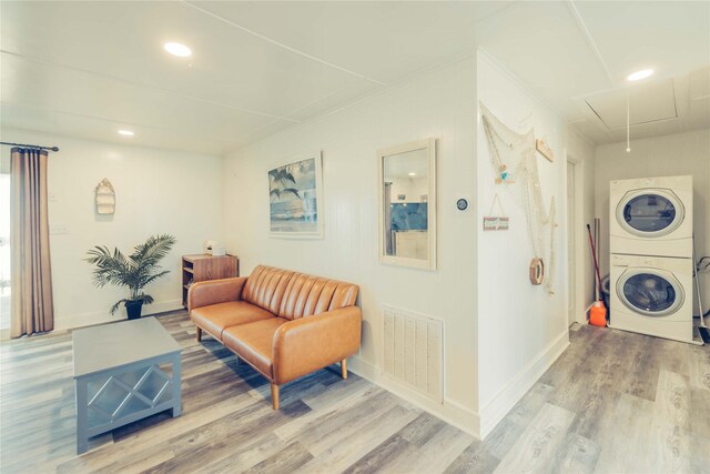 clothes washing area featuring stacked washing machine and dryer, attic access, wood finished floors, baseboards, and recessed lighting