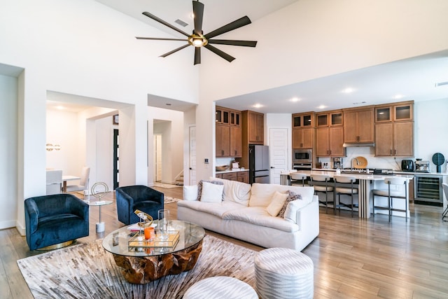 living room with ceiling fan, beverage cooler, light wood-style floors, recessed lighting, and a high ceiling