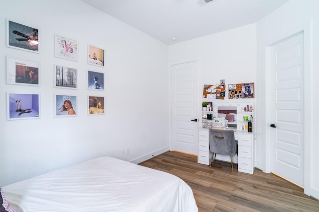 bedroom featuring wood finished floors, an office area, and baseboards