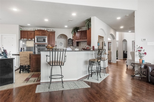 4635 Countrymeadows Dr, Spring, TX 77388 - kitchen featuring appliances with stainless steel finishes, arched walkways, light wood finished floors, a kitchen bar, and a peninsula