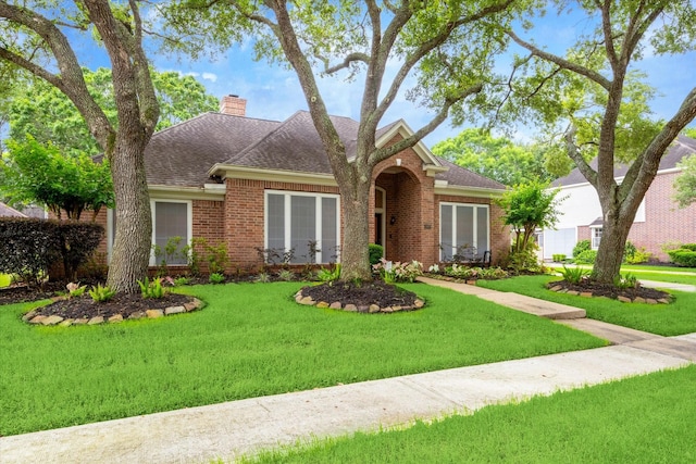 view of front of house with brick siding, a front lawn, a chimney, and a shingled roof
