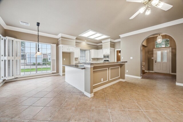 kitchen with stainless steel microwave, light tile patterned flooring, arched walkways, and ornamental molding