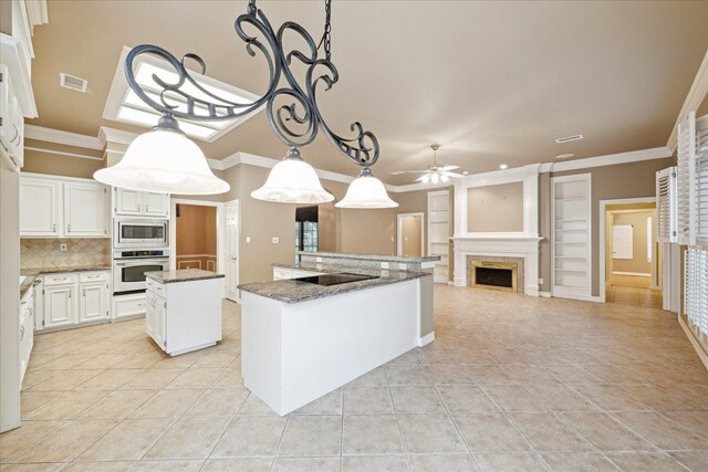 kitchen featuring wall oven, stainless steel microwave, a kitchen island, a ceiling fan, and light tile patterned floors