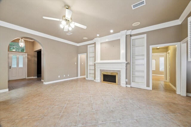 unfurnished living room featuring arched walkways, ceiling fan, built in features, baseboards, and ornamental molding