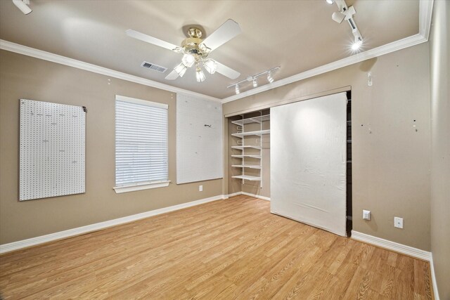 unfurnished bedroom featuring track lighting, wood finished floors, ornamental molding, a closet, and baseboards