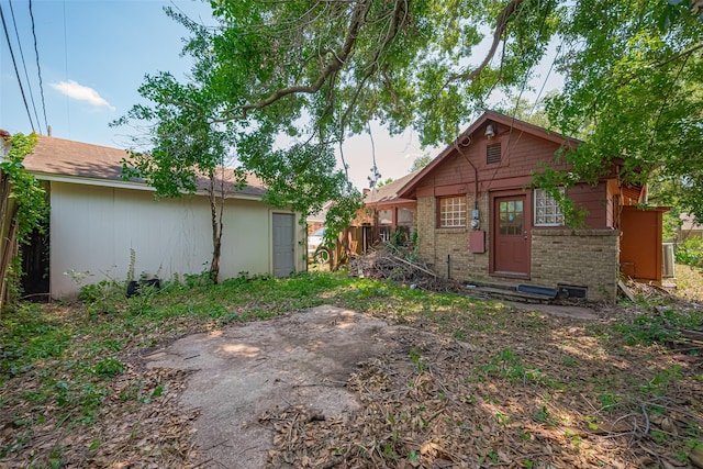 back of house with brick siding, fence, entry steps, and an outbuilding