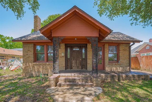 view of front of home with fence, a chimney, brick siding, and roof with shingles