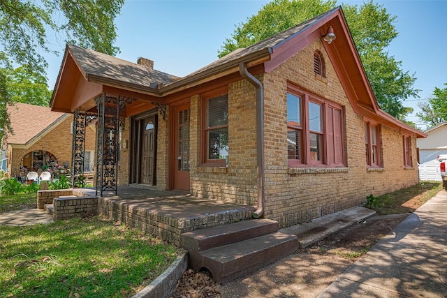 view of front of property with brick siding, a chimney, and roof with shingles
