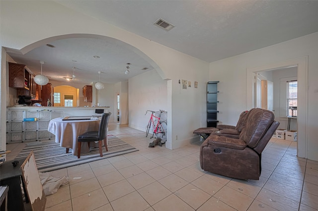 living area with arched walkways, healthy amount of natural light, light tile patterned floors, and baseboards