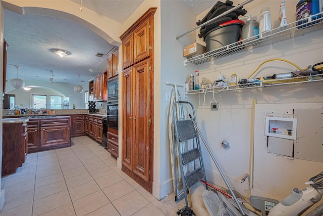 kitchen featuring arched walkways, a textured ceiling, light tile patterned floors, black microwave, and a peninsula