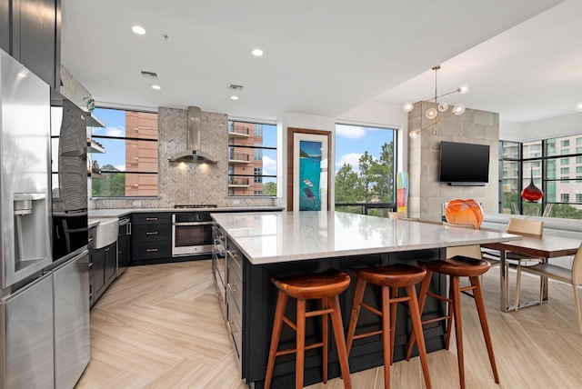 1 Waterway Ct Unit 4B, The Woodlands, TX 77380 - kitchen with wall chimney exhaust hood, stainless steel appliances, a spacious island, light stone countertops, and dark cabinetry