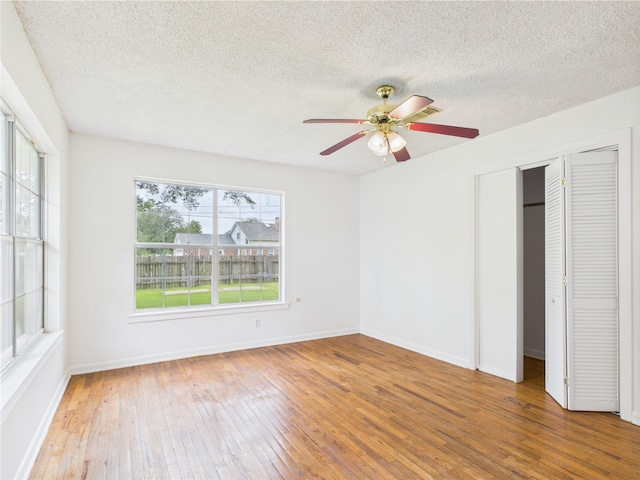 unfurnished bedroom with wood-type flooring, a textured ceiling, baseboards, a closet, and ceiling fan