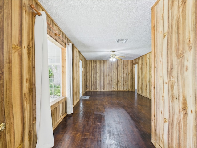 unfurnished room featuring dark wood finished floors, ceiling fan, a textured ceiling, and wooden walls