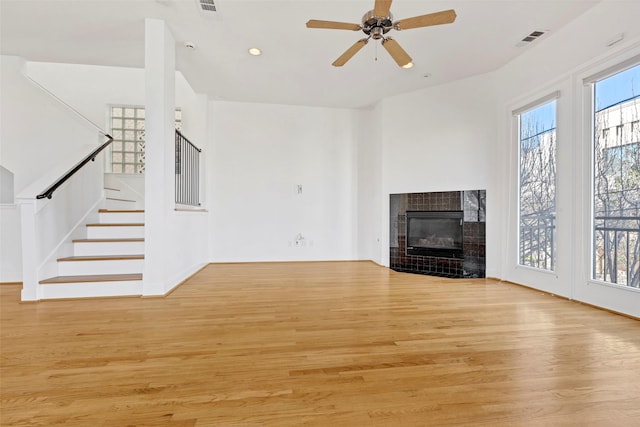 unfurnished living room with light wood finished floors, stairway, ceiling fan, a tiled fireplace, and recessed lighting