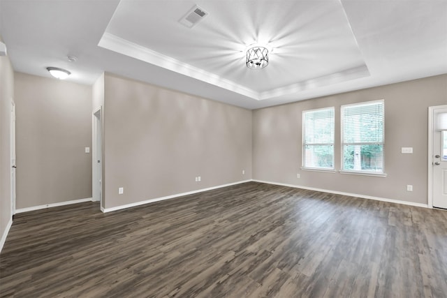 unfurnished living room featuring a raised ceiling, dark wood-type flooring, baseboards, and ornamental molding