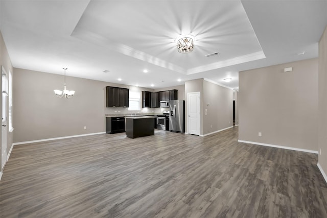 unfurnished living room with a raised ceiling, a chandelier, baseboards, recessed lighting, and crown molding