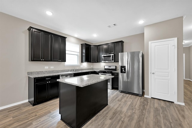 kitchen with stainless steel appliances, dark cabinets, light wood finished floors, light stone counters, and recessed lighting