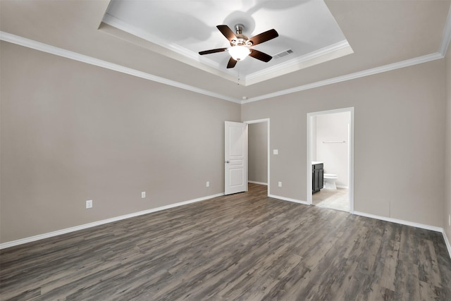unfurnished bedroom with a tray ceiling, dark wood finished floors, ensuite bath, baseboards, and crown molding