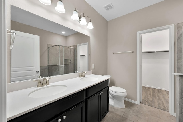 full bath featuring a shower stall, a spacious closet, double vanity, toilet, and baseboards