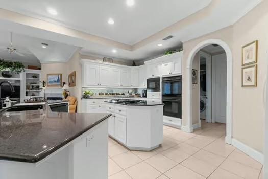 2 Argonne Pl, The Woodlands, TX 77382 - kitchen featuring a kitchen island with sink, black appliances, a sink, stacked washer / dryer, and white cabinetry