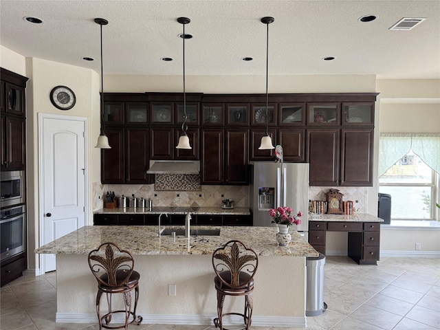24130 Cannon Anello Ct, Katy, TX 77493 - kitchen featuring appliances with stainless steel finishes, tasteful backsplash, a kitchen breakfast bar, glass insert cabinets, and hanging light fixtures