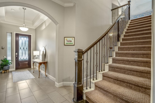 foyer with arched walkways, stairs, ornamental molding, baseboards, and a tray ceiling