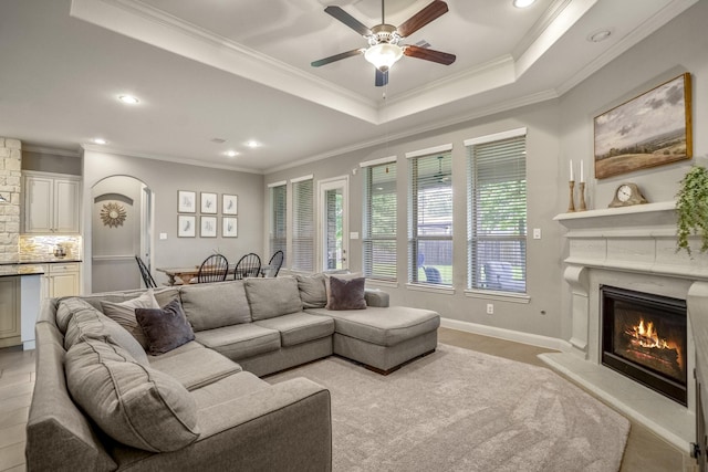 living area with a ceiling fan, a glass covered fireplace, arched walkways, recessed lighting, and ornamental molding