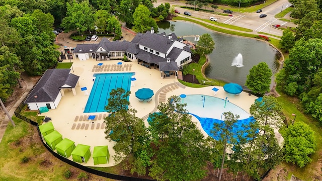 aerial view of a pool, a large body of water, and a tree filled landscape