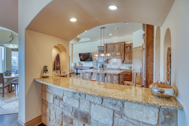 143 Westgate Loop, Horseshoe Bay, TX 78657 - kitchen with light stone countertops, brown cabinetry, decorative backsplash, recessed lighting, and arched walkways