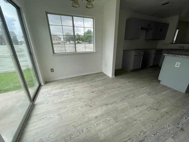 unfurnished dining area with light wood-style floors, a chandelier, a sink, and baseboards