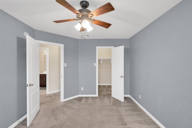 unfurnished bedroom with light carpet, baseboards, a spacious closet, ceiling fan, and a closet