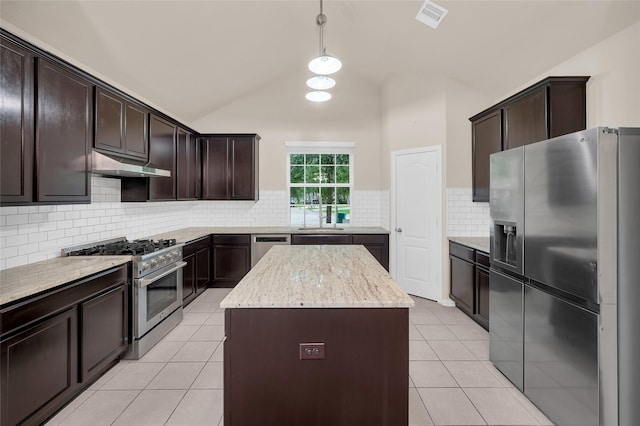 kitchen with appliances with stainless steel finishes, under cabinet range hood, a kitchen island, light tile patterned floors, and dark brown cabinetry