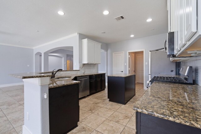 19107 Egret Glen Ct, Cypress, TX 77429 - kitchen with appliances with stainless steel finishes, a sink, a kitchen island, arched walkways, and dark stone countertops