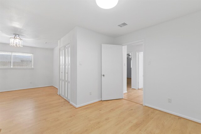 empty room featuring light wood finished floors, baseboards, and a chandelier