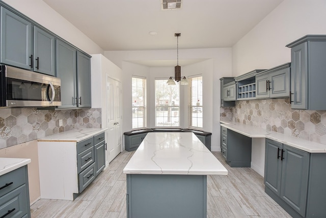 1049 Misty Clf, Dickinson, TX 77539 - kitchen with stainless steel microwave, a kitchen island, light wood-style flooring, and gray cabinetry