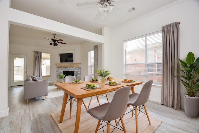 1049 Misty Clf, Dickinson, TX 77539 - dining space with ceiling fan, a stone fireplace, light wood-style flooring, baseboards, and crown molding
