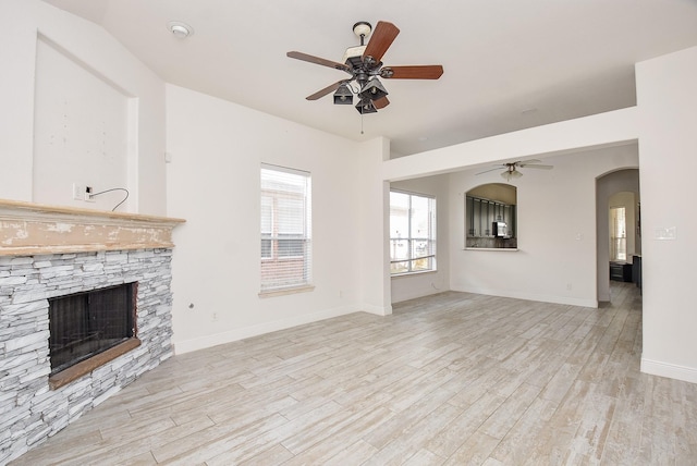 1049 Misty Clf, Dickinson, TX 77539 - unfurnished living room featuring a ceiling fan, a stone fireplace, light wood-type flooring, and arched walkways