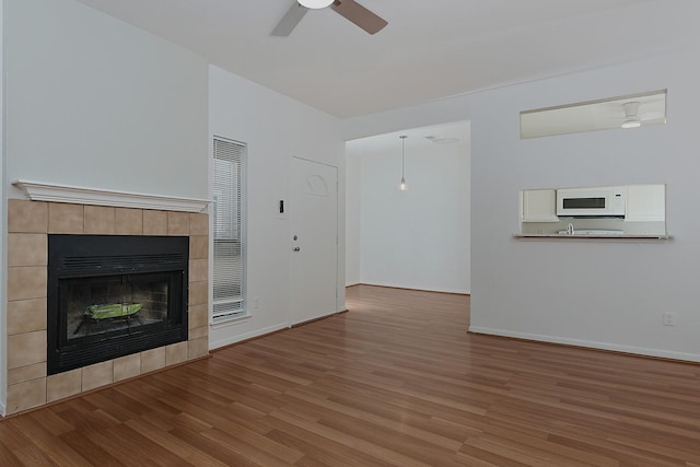 3500 Tangle Brush Dr Unit 217, The Woodlands, TX 77381 - unfurnished living room featuring wood finished floors, ceiling fan, a tiled fireplace, and baseboards