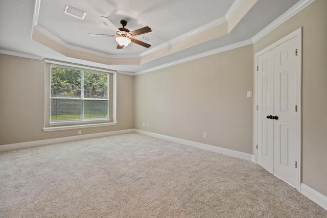 empty room with a raised ceiling, a ceiling fan, ornamental molding, carpet floors, and baseboards