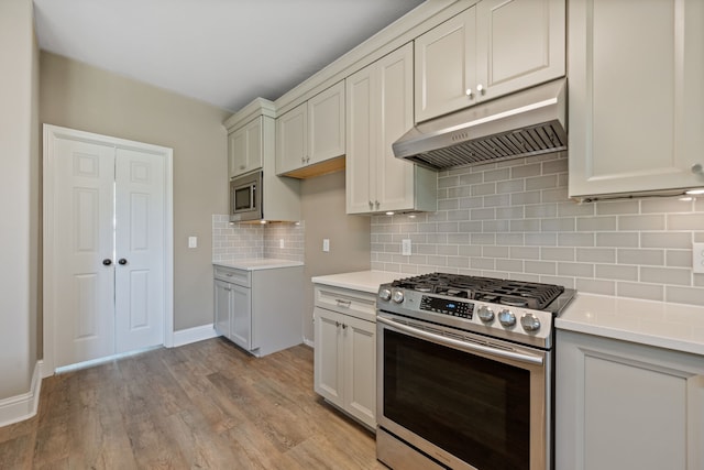 kitchen with appliances with stainless steel finishes, under cabinet range hood, light countertops, and light wood-style floors